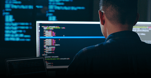 Person coding on computer screens in dark.