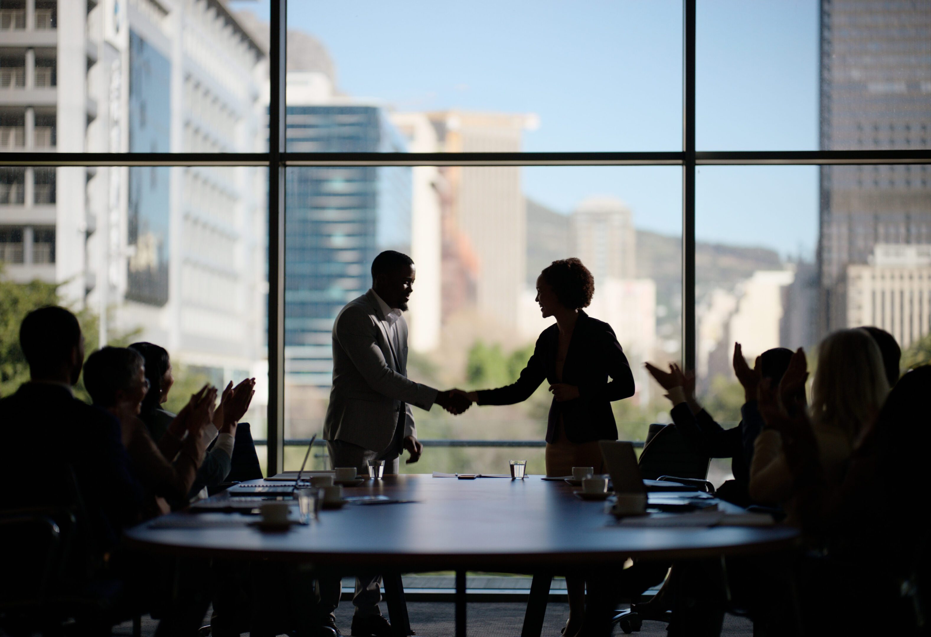 Silhouetted handshake in meeting room, applauding audience.