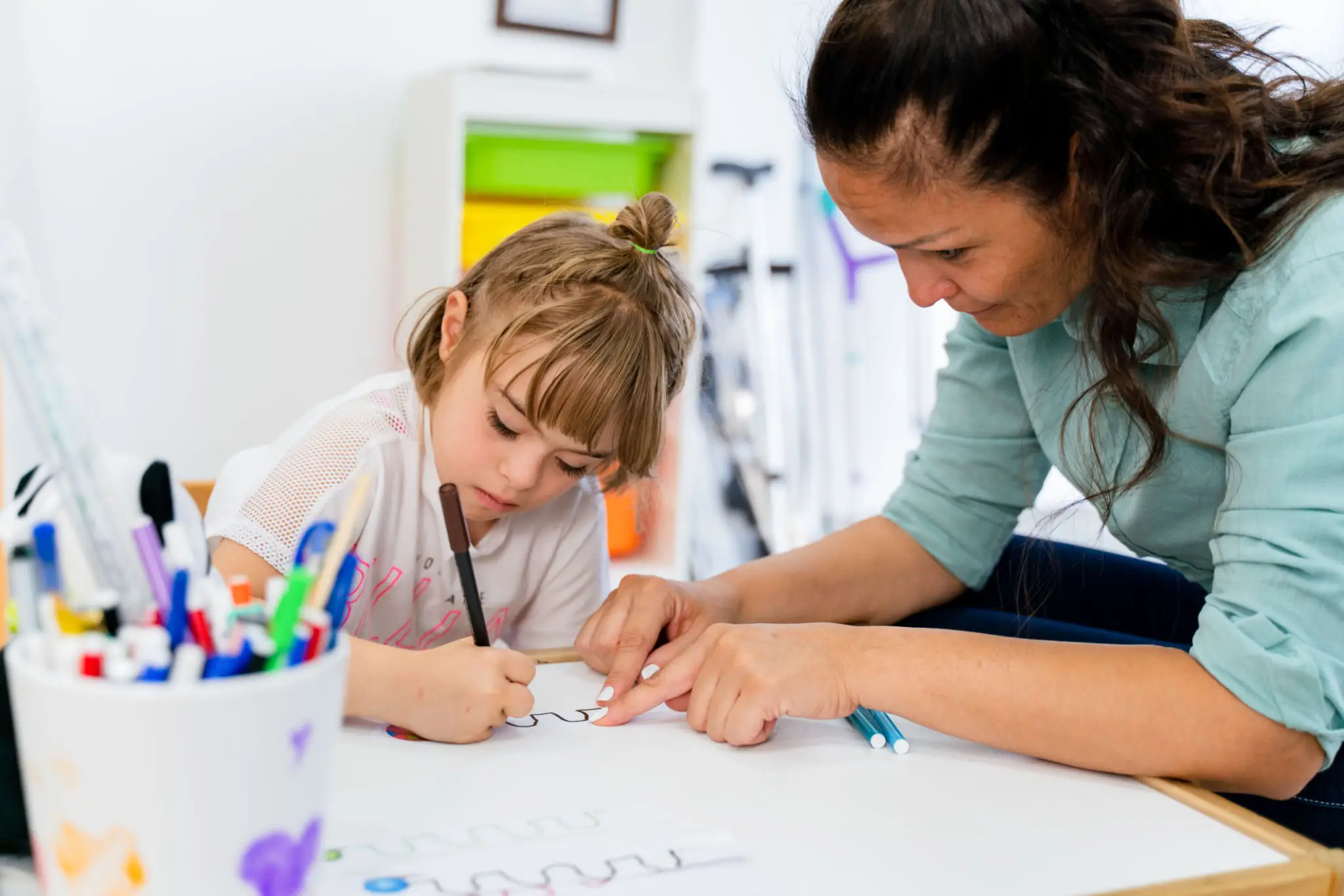 Woman helping child draw at table